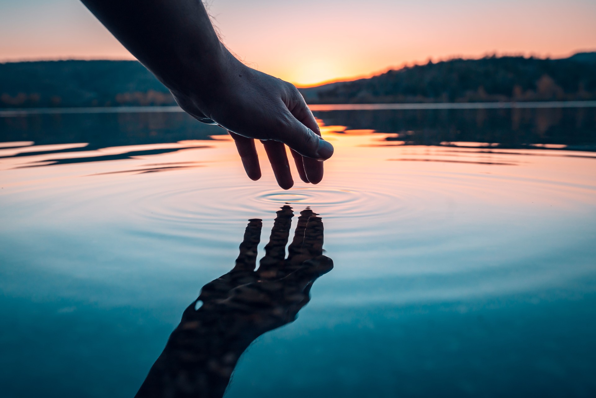 Dedo toque la superficie del lago de la montaña. Reflexión de la mano